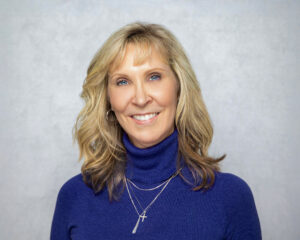 Dr. Susan Bushelman, the board-certified dermatologist who leads our skin clinic in Florence, wears a blue turtleneck sweater while smiling to the camera.