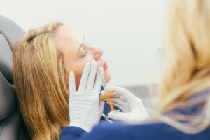 A close up of a female Dermatology Aestheticsof Northern Kentucky provider injects dermal filler into her nasal lines. Filler near Cincinnati can also minimize the appearance of marionette lines, hollow cheeks, or thinning lips.