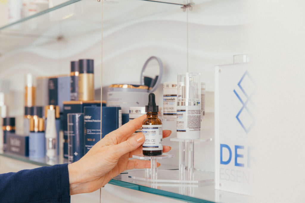 A hand reaches onto a shelf with medical-grade skincare products and picks up a serum to pair with dermal fillers for under eyes near Cincinnati, enhancing their results.